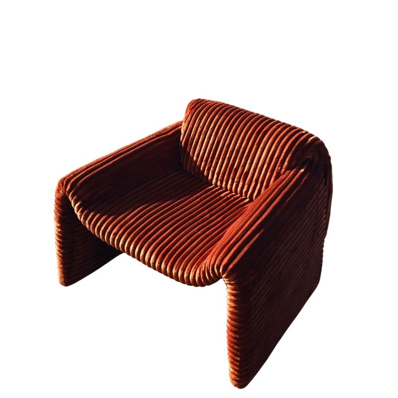 Rust orange ribbed velvet armchair with a sculptural design on a wooden deck by the sea. Mahogni