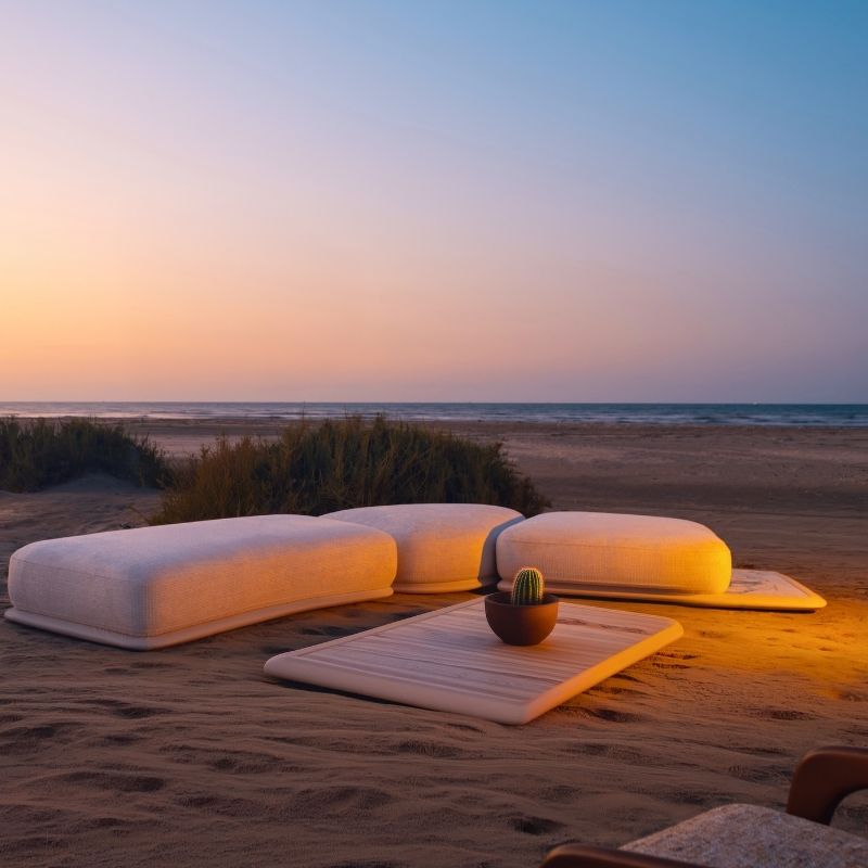 Minimalist cream floor seating set with organic rounded ottomans on sand at sunset.