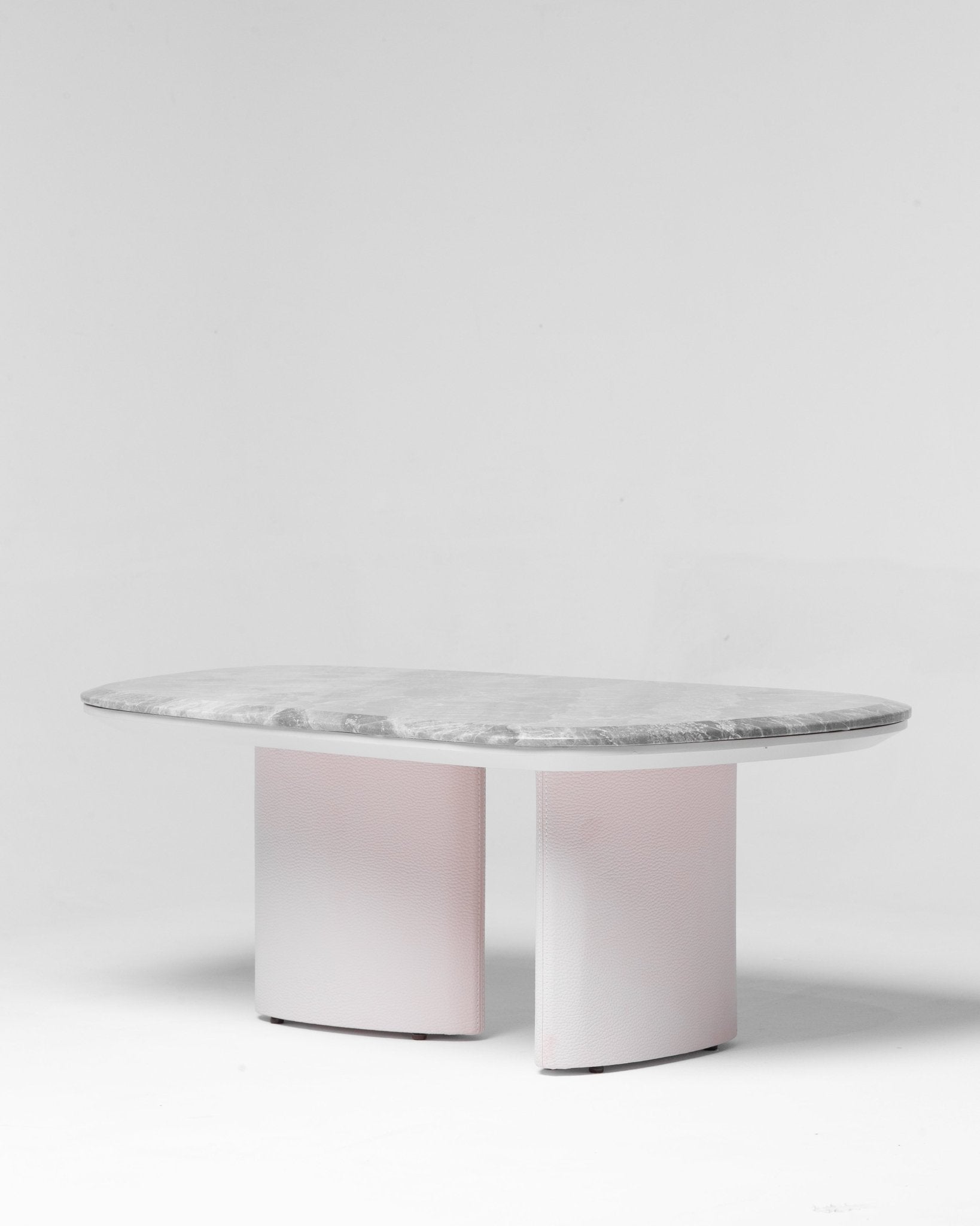Contemporary oval dining table featuring a thick grey marble top and light pink textured pedestal base by Mahogni.