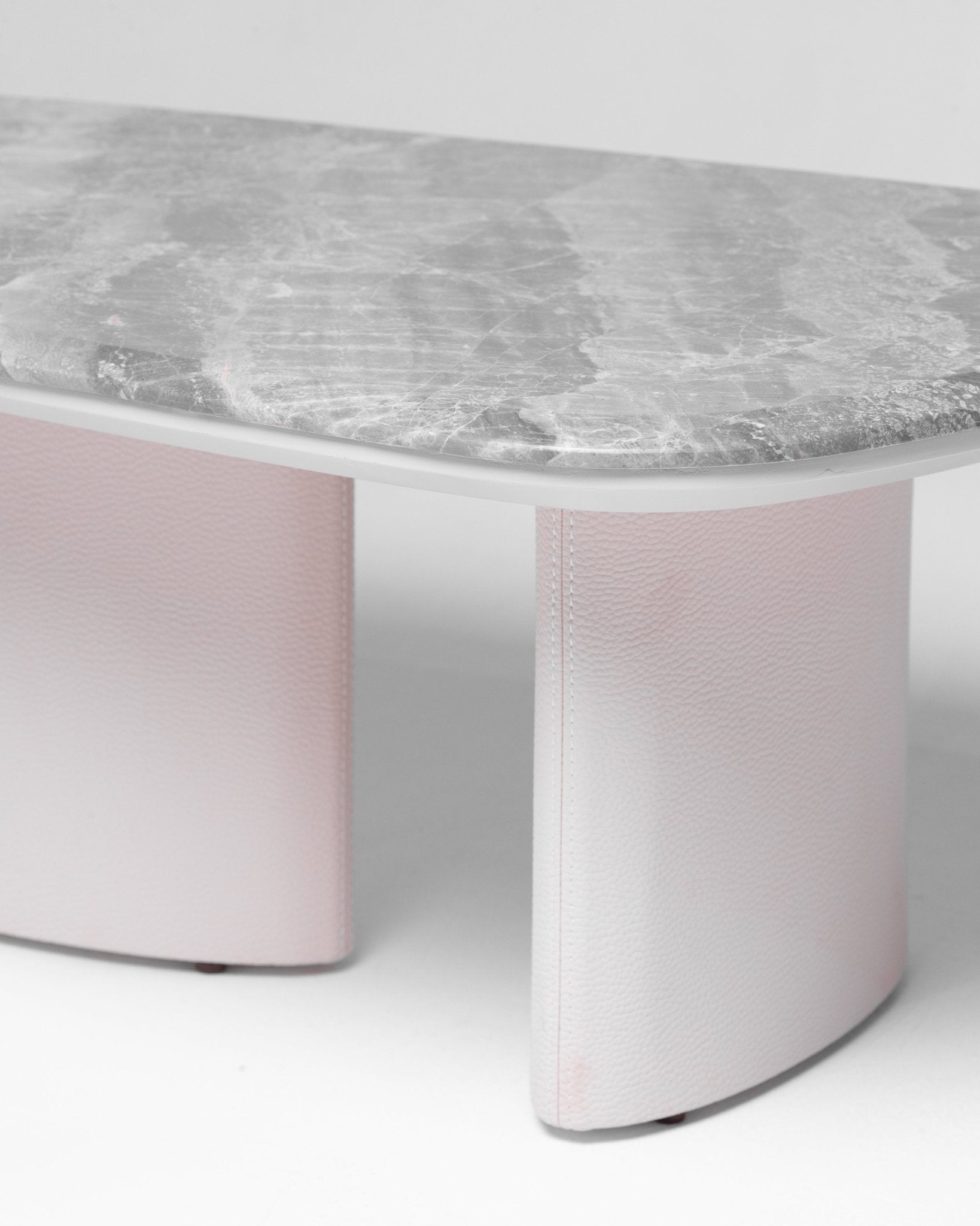 Contemporary oval dining table featuring a thick grey marble top and light pink textured pedestal base by Mahogni.
