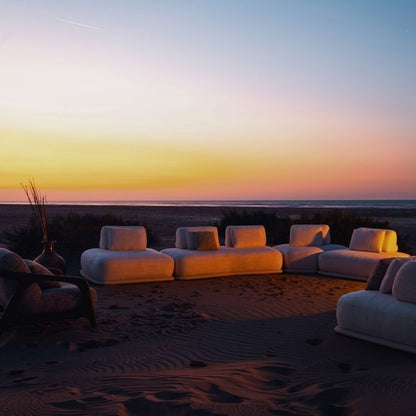 Luxury white bouclé modular sofa set with rounded cushions on a carpeted outdoor lounge at sunset. Mahogni 