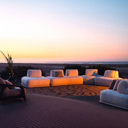 Luxury white bouclé modular sofa set with rounded cushions on a carpeted outdoor lounge at sunset. Mahogni 