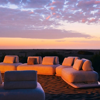 Luxury white bouclé modular sofa set with rounded cushions on a carpeted outdoor lounge at sunset. Mahogni 