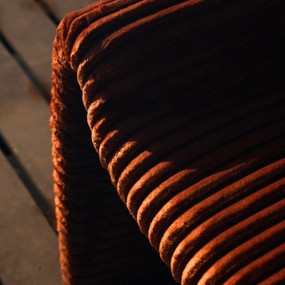Rust orange ribbed velvet armchair with a sculptural design on a wooden deck by the sea.