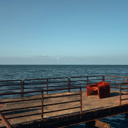 Rust orange ribbed velvet armchair with a sculptural design on a wooden deck by the sea. Mahogni