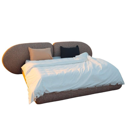 Minimalist organic shaped bed with a stone-like texture and curved headboard on a wooden pier at sunset. Mahogni 