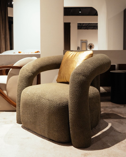 Modern aura sculptural accent chair in olive grey boucle fabric with gold satin pillow by Mahogni furniture.