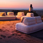 Luxury white bouclé modular sofa set with rounded cushions on a carpeted outdoor lounge at sunset. Mahogni 
