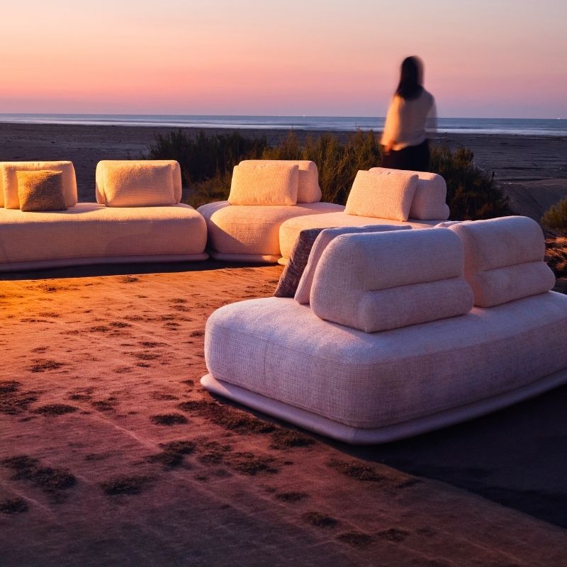 Luxury white bouclé modular sofa set with rounded cushions on a carpeted outdoor lounge at sunset. Mahogni 