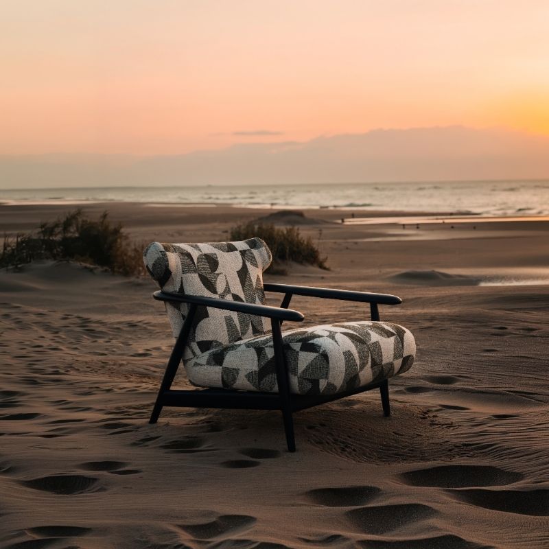 Complete modular living room sofa set in pebble grey with charcoal geometric pillows on a sandy backdrop at sunset. Mahogni 