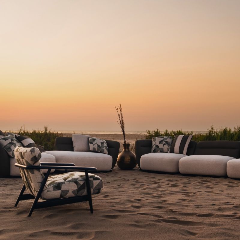 Complete modular living room sofa set in pebble grey with charcoal geometric pillows on a sandy backdrop at sunset.