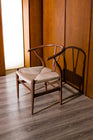 Mid-century modern wishbone chair made of rich walnut-finished wood with a hand-woven natural cord seat, set against a warm wooden wall background