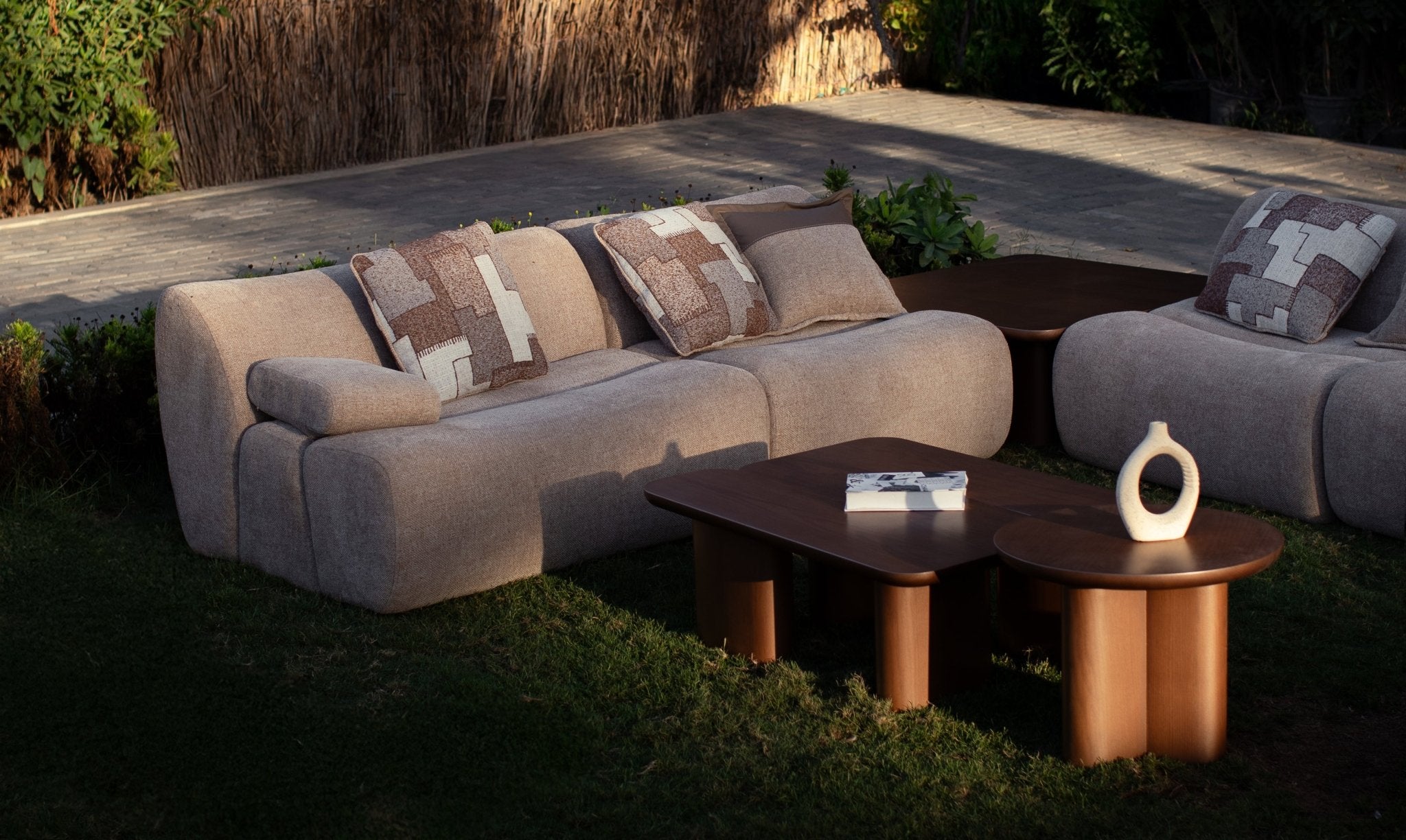 Soft living room set featuring a large modular sectional in warm beige textured fabric with geometric patterned cushions and dark wood coffee tables by Mahogni 