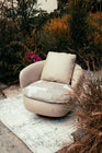 Swivel Chair by Mahogni - Rounded tub-style armchair with beige fabric and a natural wooden swivel base in a lush outdoor garden setting.