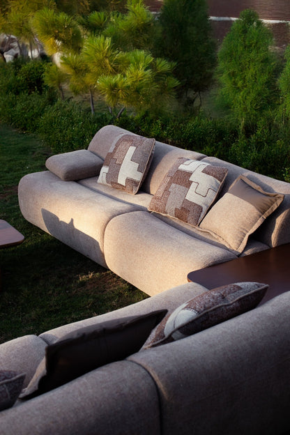 Soft living room set featuring a large modular sectional in warm beige textured fabric with geometric patterned cushions and dark wood coffee tables by Mahogni 