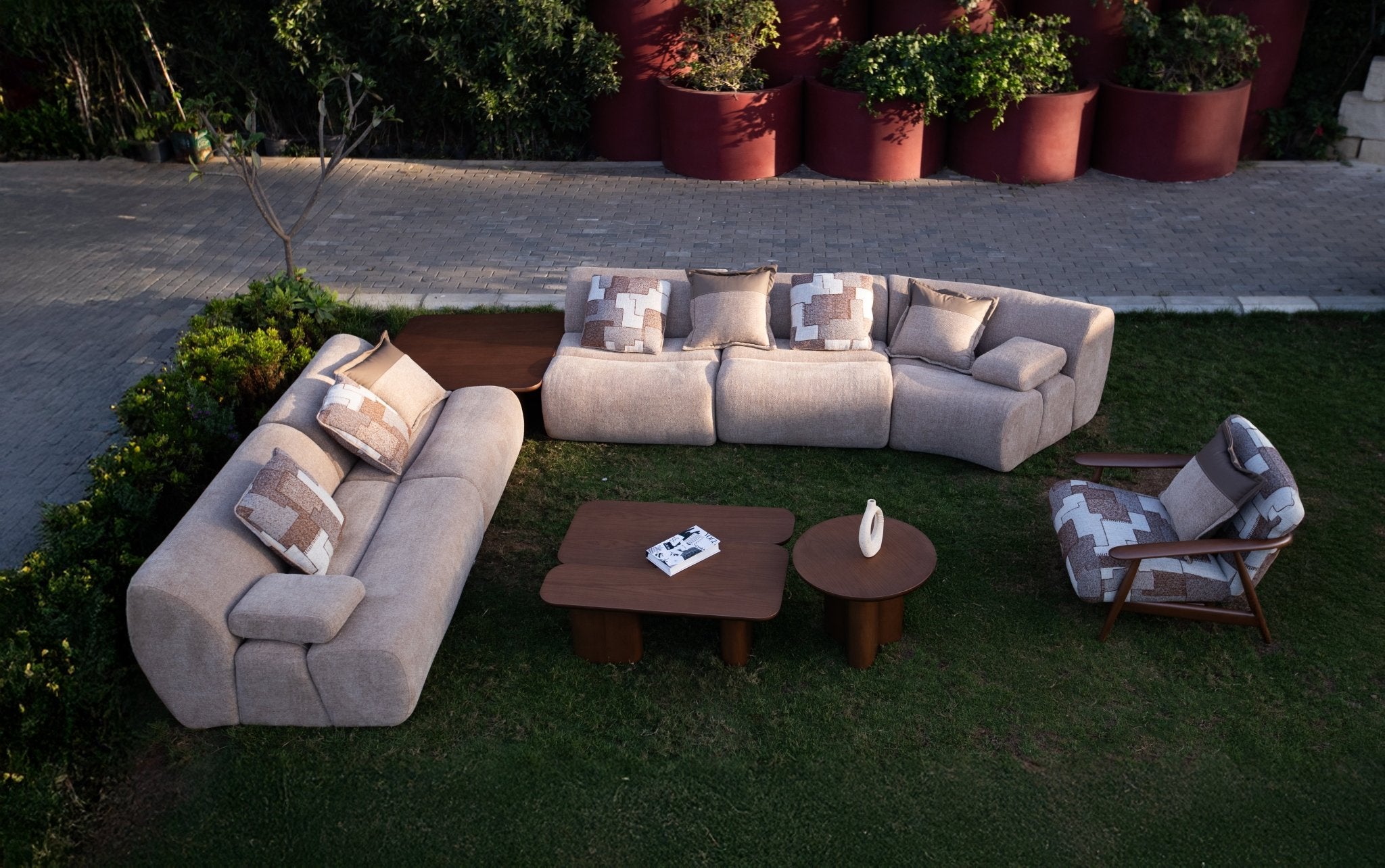 Soft living room set featuring a large modular sectional in warm beige textured fabric with geometric patterned cushions and dark wood coffee tables by Mahogni 